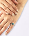 Hand wearing a ring with a green gemstone on a light background